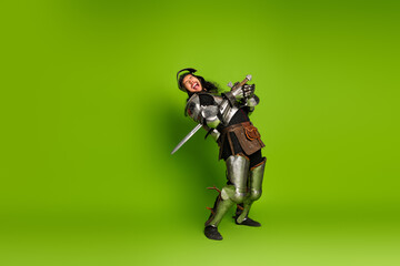 Young male in medieval knight costume with comedic expression against green backdrop, evoking...