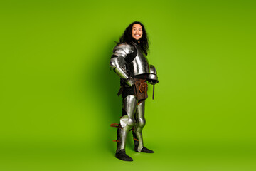 Handsome young man posing confidently in medieval knight costume and armor on vibrant green backdrop