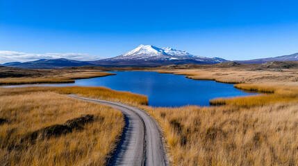 Scenic mountain lake with winding road and autumnal grasses under a clear blue sky