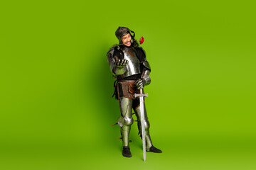 Young man in medieval knight costume on green background holding a sword