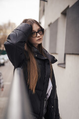 Naklejka premium Stylish young woman in a black jacket on a city street on a cool day