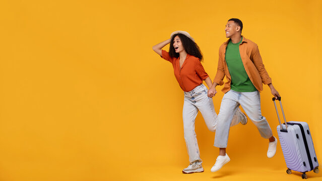 Travel ad. Excited African American couple running with luggage and looking at copy space on orange background, ready for vacation trip, panorama