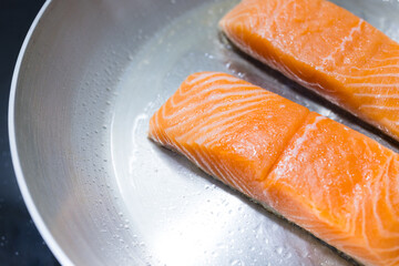 Two raw salmon fillets frying on stove