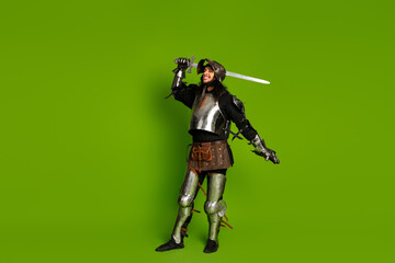 Fototapeta premium Medieval knight in full armor holding a sword on a vibrant green background