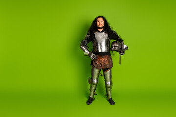 Young man in medieval knight armor on a green background showcasing historical costume