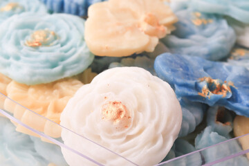 Colorful flower shaped Thai desserts with gold leaf accents are beautifully arranged, showcasing intricate details and vibrant hues. delicate craftsmanship and pastel colors create elegant