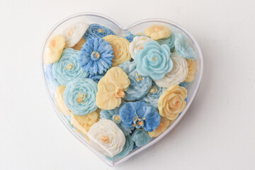 Fototapeta premium Heart shaped container filled with colorful, intricately designed flower shaped soaps in shades of blue, yellow, and white, creating visually appealing and fragrant display