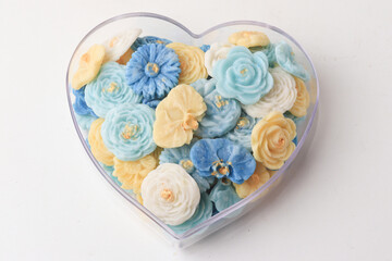 heart shaped container holds assortment of colorful, intricately designed flower shaped soaps in shades of blue, yellow, and white, creating visually appealing and fragrant display