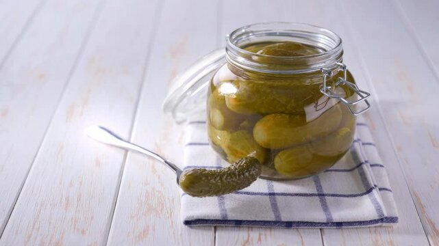 pickled cucumbers in a jar on a white wooden table. Tasty marinated cucumbers in jar on a wooden table.
