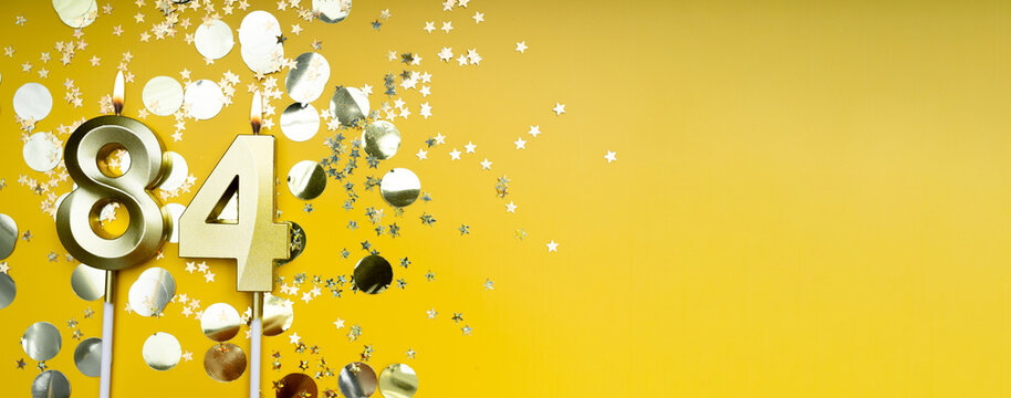 Eighty-four years birthday. Number 84 golden celebration candle. Yellow festive background. Concept of celebrating birthday or anniversary. Banner.