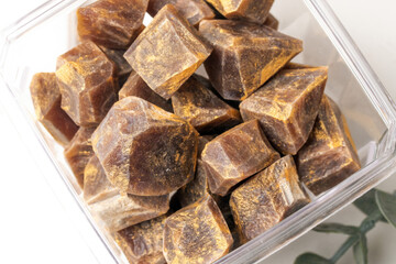 clear container filled with brown, sugar like cubes, possibly jaggery, is shown. cubes have rustic, unrefined appearance, suggesting natural sweetener. image conveys sense of organic and wholesome