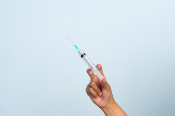 Asian woman's hand holding an injection on a white background. The hand holds a syringe.