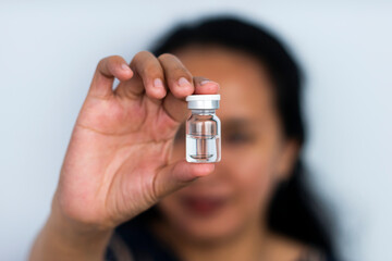 Nurse's hand with medicine prepared for vaccination, on a white background. Home nurse's hand is holding a vial containing a corneal film, eye lens in a vial.