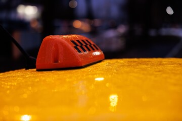 Taxi light glowing under raindrops while city lights shimmer at twilight hour