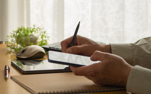 hands of a man operating a smartphone and writing on a tablet.  - Powered by Adobe