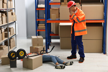 Accident at work. Worried man and his unconscious colleague in warehouse