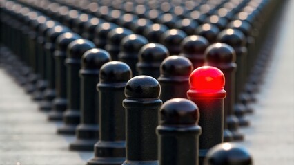 A row of black bollards, with one prominently lit red, creating a striking visual contrast in the urban landscape.