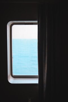 Fototapeta A serene view of the ocean seen through a window with a curtain. The calm blue water stretches beyond the frame, creating a peaceful atmosphere from inside a ship or cabin.