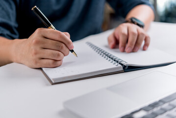 Hand writing on spiral notebook with pen and laptop, concept of education, online learning,...