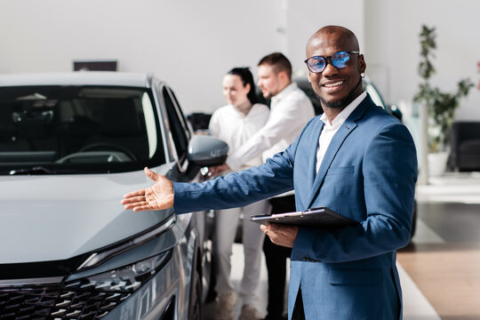 Happy, married couple during the purchase of a modern, new car accompanied by a black car dealer at a car dealership. The concept of a long-awaited purchase, sale and test drive of a new car. - Powered by Adobe