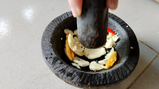 Hands using a mortar and pestle to crush garlic and chilies, illustrating traditional cooking methods. Fresh ingredients and manual preparation bring natural flavors to culinary dishes.