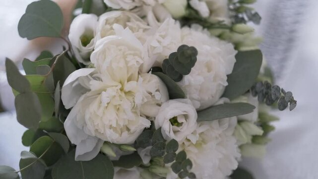 Close-up of a white wedding bouquet with peonies, lisianthus and eucalyptus leaves on a soft textured surface


