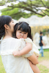 Naklejka premium Mother carries daughter in park,Happy young caucasian mother and toddler girl daughter look at the camera and smiling, summer park on background