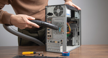 Man cleans a computer case with a vacuum cleaner.