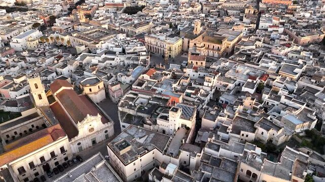 Aerial drone view of Nardo, a historic town in southern Italy, bathed in golden sunset light. The old towns dense architecture, whitewashed buildings, and narrow streets highlight its rich cultural