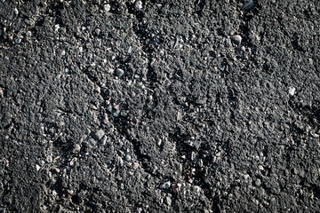 close-up of cracked weathered asphalt. The asphalt is dark and coarse, with visible pebbles and small stones embedded background