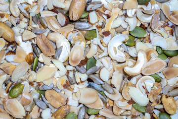 A vibrant mix of nuts and seeds, including cashews, almonds, and pumpkin seeds, is scattered across a white surface, showcasing a healthy and natural snack.