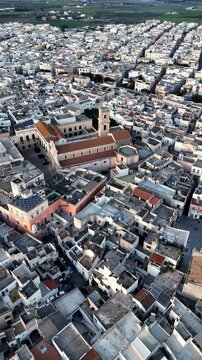Aerial drone view of Nardo, a historic town in southern Italy, bathed in golden sunset light. The old towns dense architecture, whitewashed buildings, and narrow streets highlight its rich cultural