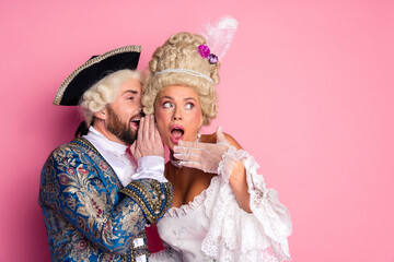 Elegant couple in royal costumes sharing secrets at a carnival themed party with a pink background