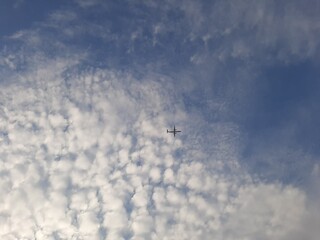 A small airplane flies high in the sky against a backdrop of scattered white clouds. A peaceful aerial view capturing the beauty of aviation and nature.