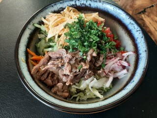 A bowl of fresh Asian-style salad with beef, vegetables, egg strips, and herbs. A colorful, healthy dish full of flavor and texture.