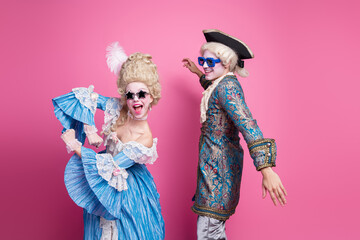 Colorful couple dressed in glamorous baroque costumes at a themed party against vibrant pink...