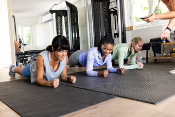 Diverse female friends exercising in gym, doing planks on mats, focused and determined, at home