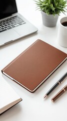 Fototapeta premium Workspace featuring a brown notebook, laptop, coffee cup, and plant in a minimalistic setting during a bright day