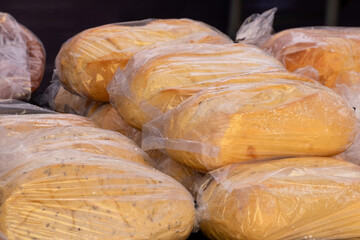 A display of artisan breads in clear plastic bags for sale at a farmer's market. The crusty, sourdough, pumpernickel, white, whole wheat, and traditional homemade rustic loaves are on display for sale