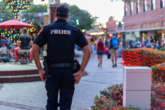 Orlando, Florida, USA-March 1, 2025: A male police officer walking along a sidewalk in a downtown area is wearing a taser and hand gun. The law enforcement officer wears a black bullet proof vest.  
