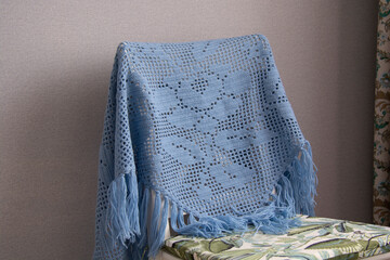 A blue shawl knitted using the fillet knitting technique hangs on a white chair