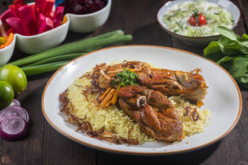 Mandi Rice with Meat served on a white plate features tender meat, aromatic rice, and various side dishes isolated on wooden table side view of a gourmet Arabian platter