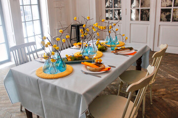 Easter table setting in yellow and blue colors, with yellow flowers, chickens on branches and blue vases