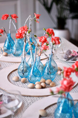modern Easter table setting with blue vases, pink flowers and wooden eggs in a white interior