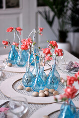 modern Easter table setting with blue vases, pink flowers and wooden eggs in a white interior