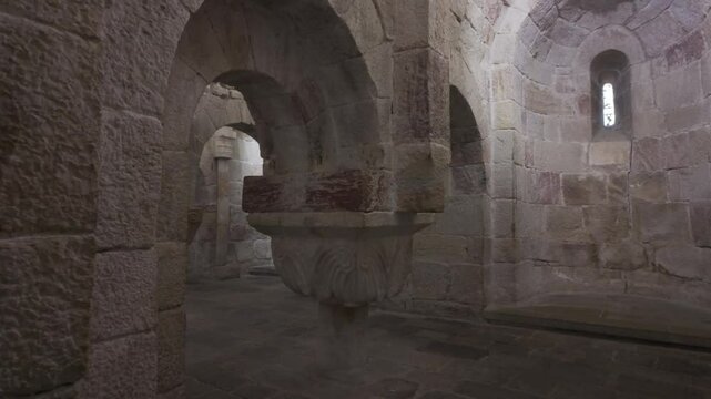 Horizontal footage moving upward from the stone floor to the vaulted ceiling inside the crypt of Leyre Monastery in Spain. The video reveals a decorated column, Romanesque arches, and a absidiole