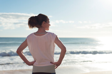 sporty woman standing by the ocean resting after exercise, looking out to sea