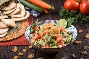 Fattoush salad served in a bowl on wooden table, features pita bread pieces, fresh vegetables, and herbs side view of healthy Middle Eastern salad