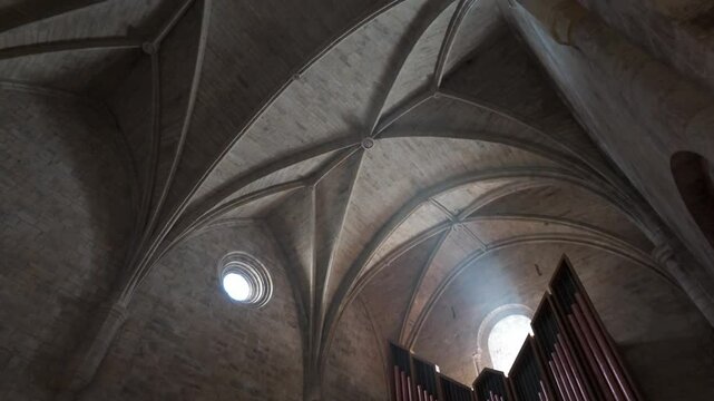 Horizontal footage panning from the stone floor up to the vaulted Gothic ceiling of the church in Leyre Monastery, Spain. The video highlights the majestic pipe organ and the gothic church