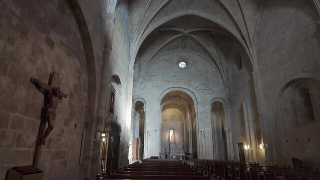 Horizontal footage panning from the floor up to the ceiling inside the church of Leyre Monastery, Spain. The scene reveals a wooden crucifix, rows of pews, the Gothic nave, and the Romanesque apse